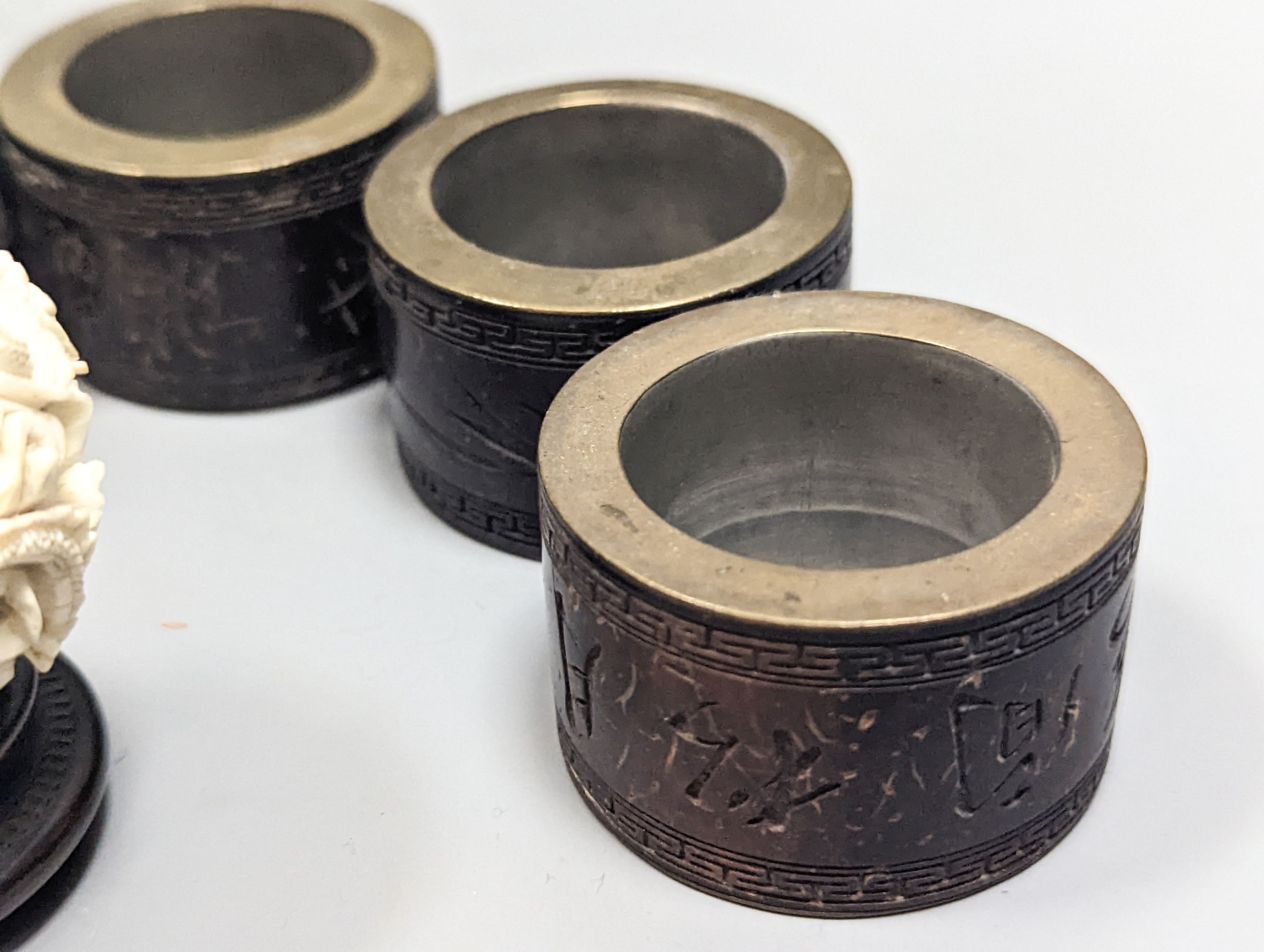 A Chinese ivory concentric puzzle ball, 6 Chinese coconut and brass mounted napkin rings.